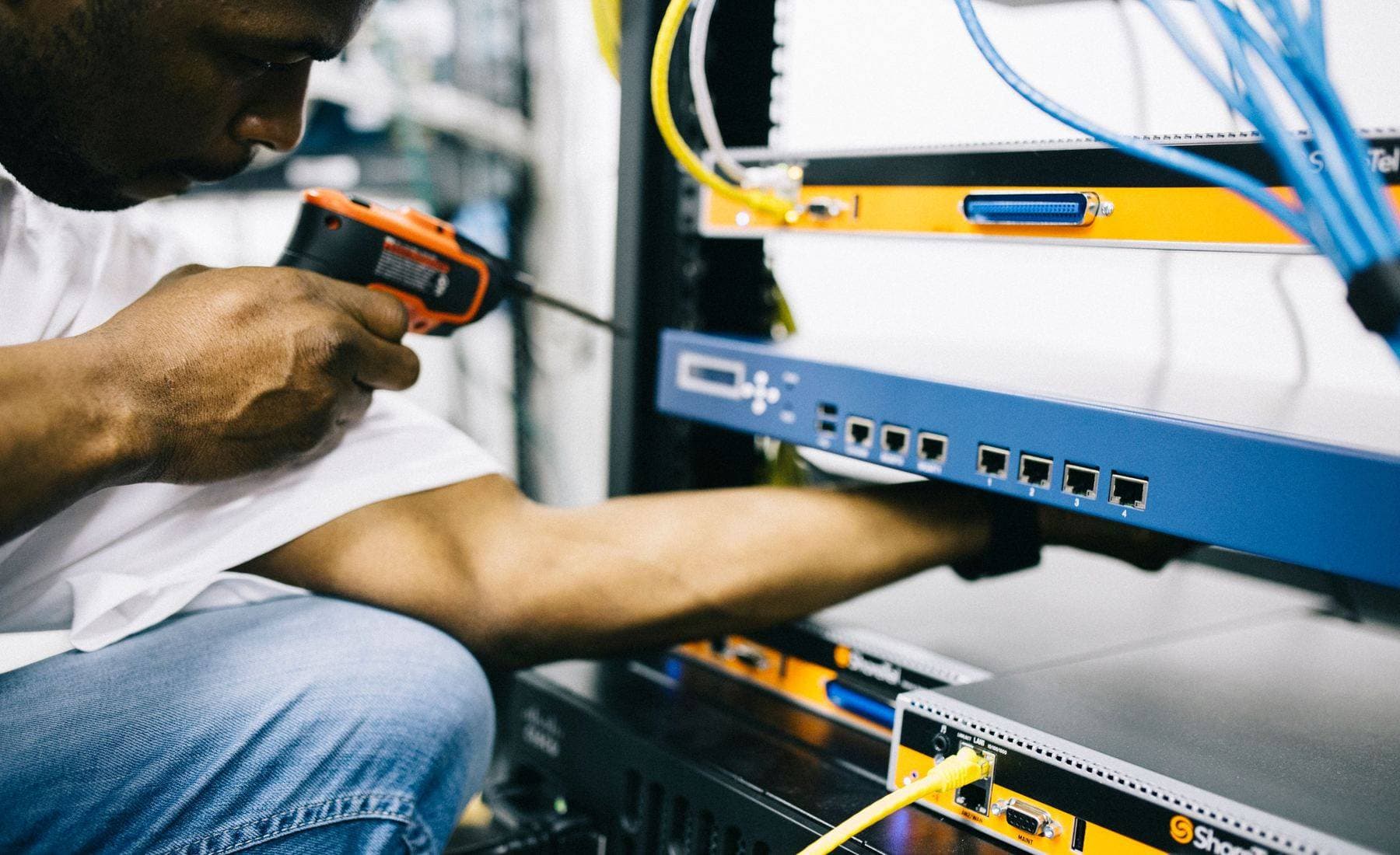 An engineer using a handheld cable tester on a network cabinet to trace a fault
