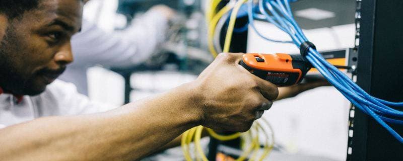 An engineer using a handheld cable tester on network cabling to trace a fault