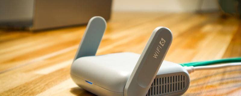 A mesh Wi-Fi access point sitting on a wooden floor beside a desk, patch lead connected